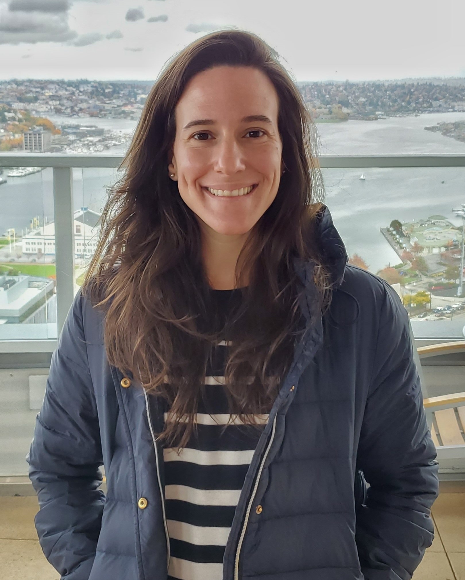 In this picture I'm smiling and wearing a stripped navy and white shirt and a navy jacket. In the background of the picture is the Lake Union.