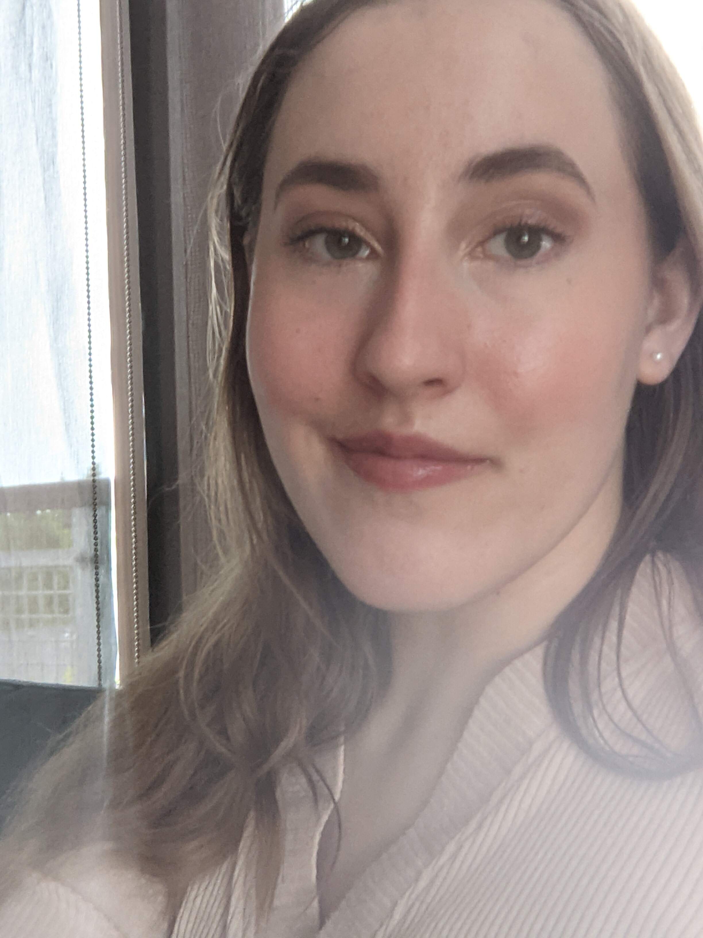 A photo of a blonde caucasian woman with thick eyebrows and green eyes wearing a beige shirt.