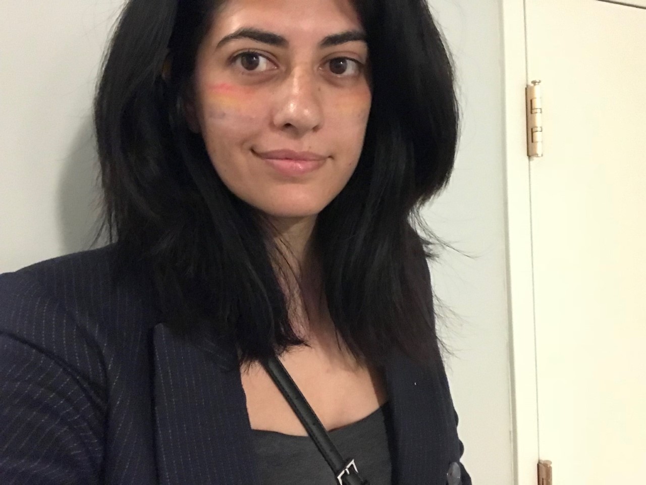 Picture of a brunette femme-presenting cis-woman wearing a dark blazer in front of a wall.
