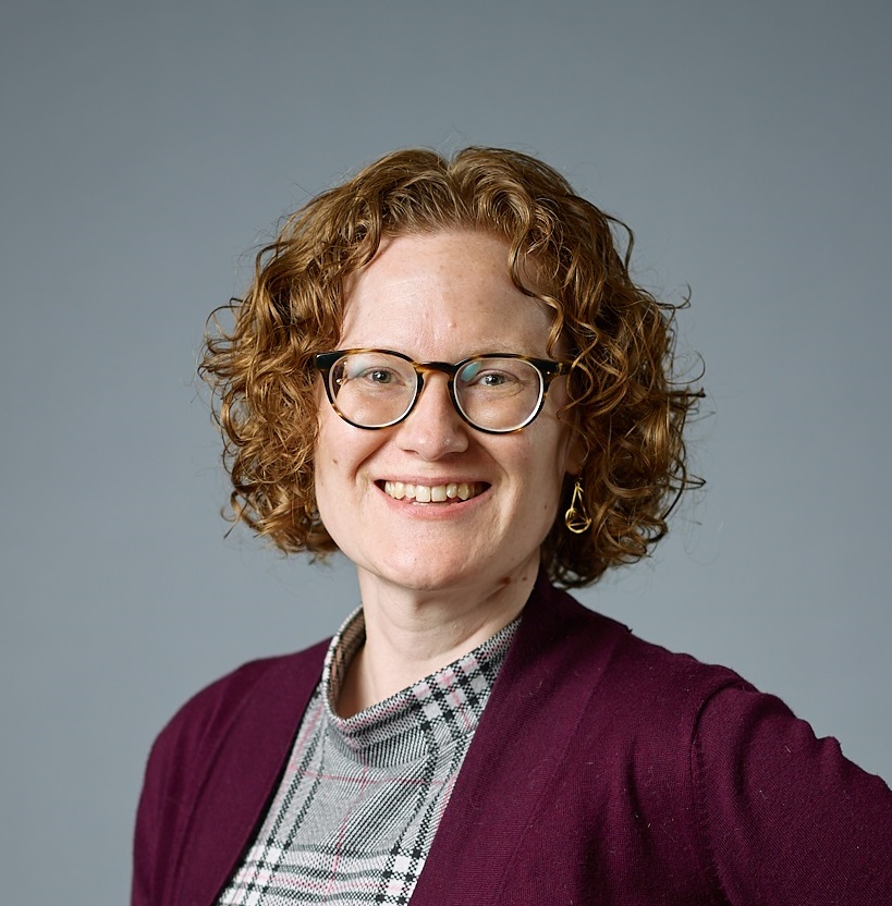 Head shot of Lisa. She is wearing a maroon sweater and has red curly hair and glasses